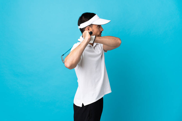 Νεαρός όμορφος άνδρας απομονωμένος σε μπλε φόντο παίζοντας γκολφ - Φωτογραφία, εικόνα