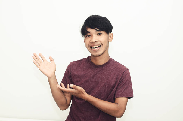 Asian man smiling in casual t-shirt while pointing at empty space - Photo, Image