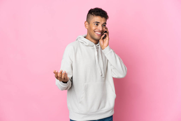 Young Brazilian man isolated on pink background keeping a conversation with the mobile phone with someone - Fotó, kép