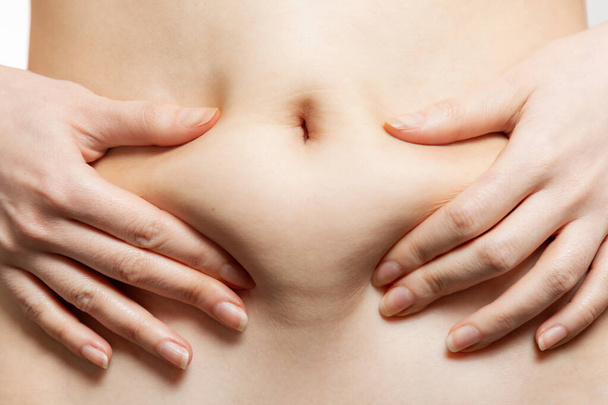 Una mujer sostiene sus manos contra su estómago, tirando de la piel con grasa. Primer plano del abdomen y el ombligo. El concepto de obesidad, pérdida de peso y liposucción. - Foto, imagen