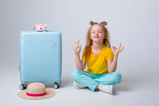 niña viajera sentada con una maleta sobre un fondo blanco - Foto, Imagen