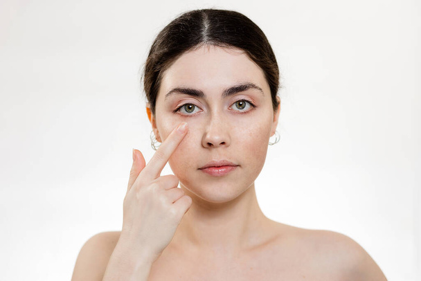 Υγεία των ματιών. Πορτραίτο μιας γυναίκας που δείχνει το δάχτυλό της στο μάτι. Λευκό φόντο. Αντιγραφή χώρου. Έννοια ελέγχου όρασης. - Φωτογραφία, εικόνα