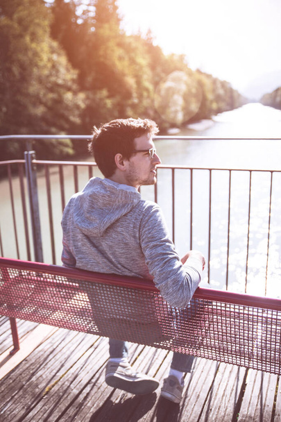 Young man is sitting on bench, enjoying the view over a river - Photo, Image