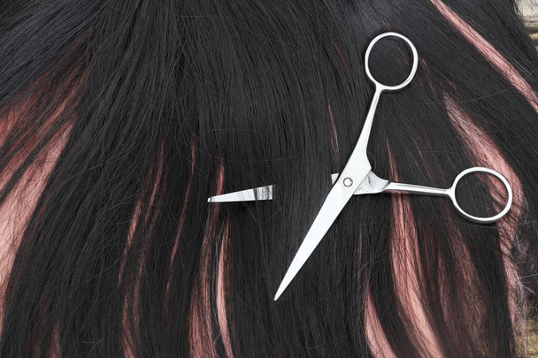 Hiusten leikkaus sakset ja musta vaaleanpunainen hiukset ruskea puu pöytä - Valokuva, kuva