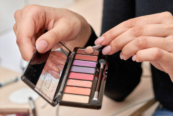 Female hands hold a set of eyeshadows and a cosmetic brush - Photo, image