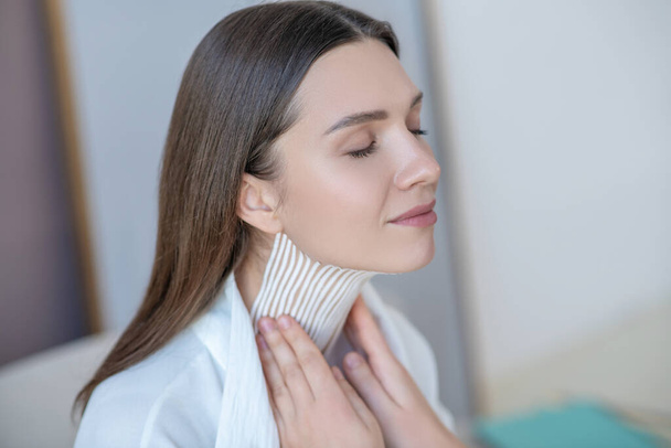 Cute young woman visiting beauty center and having taping procedure on her neck muscle - Fotografie, Obrázek