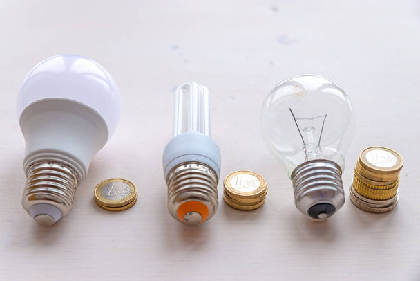 LED-lamp, gloeilamp, TL-lamp, met munten ernaast. Kosten en verbruik van de verschillende soorten gloeilampen.  - Foto, afbeelding