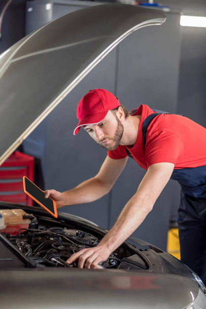 Auto mechanic with tablet examining car under hood - Foto, immagini