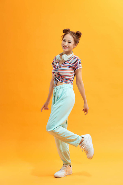 Hermosa chica asiática de pie sobre una pierna. Vista completa de la atractiva mujer japonesa elegante saltando sobre fondo púrpura. - Foto, imagen