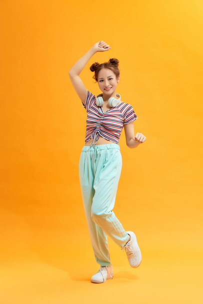 Young beautiful energy girl with white headphones listening to music laughs and jump on yellow background - Foto, Imagen
