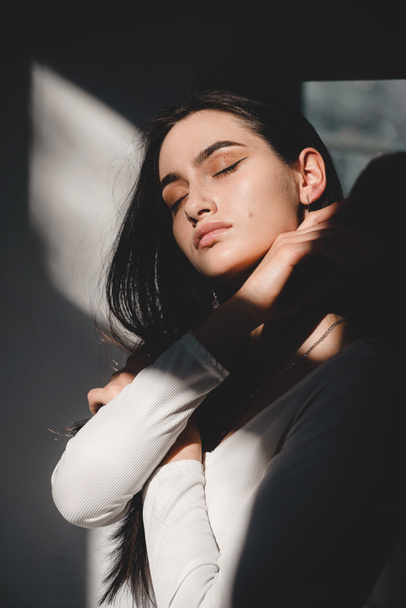 portrait of beautiful gentle woman in a white bodysuit posing in the sunshine. Black long hair. sensuality and tenderness - Photo, Image