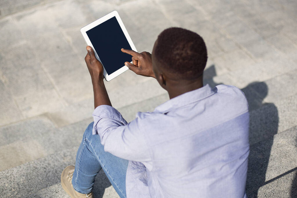 Genç siyahi adam taş merdivenlerde boş ekranlı tablet bilgisayar kullanıyor, web sitesi tasarımı için model. - Fotoğraf, Görsel