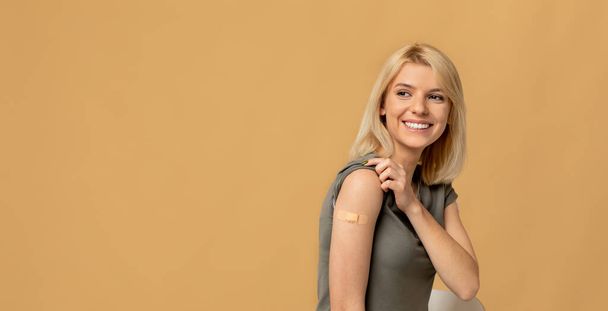 Impfungen retten Leben. Glückliche Frau, die sich gegen Covid-19 impfen lässt, posiert vor beigem Hintergrund, Panorama - Foto, Bild