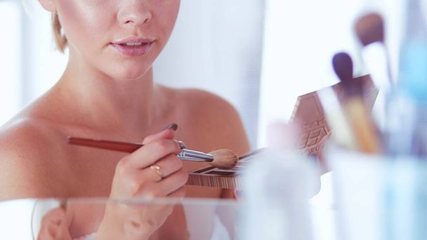 A picture of a young woman applying face powder in the bathroom - Foto, afbeelding