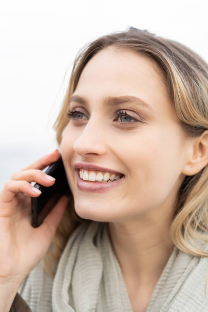 Genç, neşeli bir kadının cep telefonuyla konuşan ve soldan gülümseyen portresini yakından çek.  - Fotoğraf, Görsel