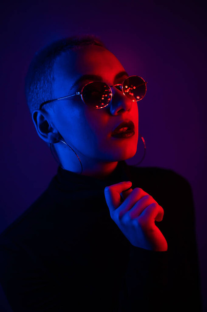Portrait of a beautiful young woman with short hair in sunglasses in neon light - Foto, Bild