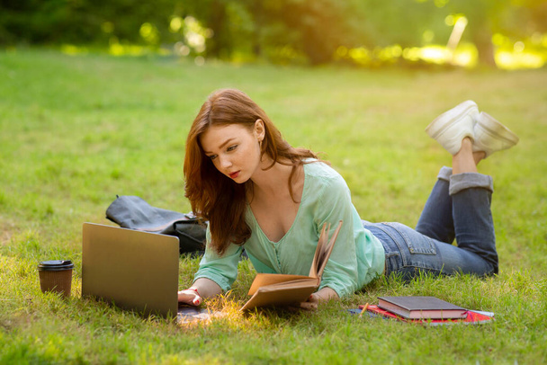 Enfocado Redhead High-School estudiante chica haciendo tarea con el ordenador portátil y libro al aire libre - Foto, imagen
