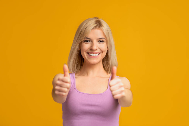 Everything is fine. Happy lady making thumb up gesture, recommending something good, yellow background - Photo, Image