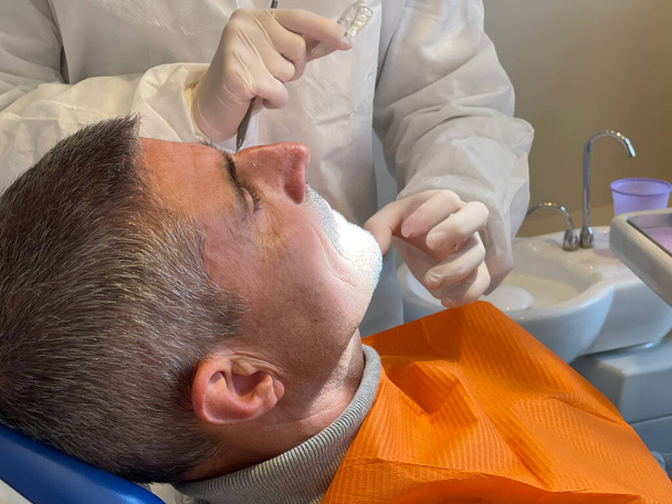 Szczęśliwy człowiek na fotelu dentysty. Dentysta pokazuje mu ugryzienie.. - Zdjęcie, obraz