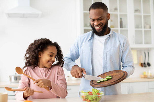 Cheerful afro father and daughter cooking salad together - Foto, Bild