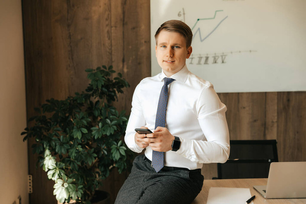 Young successful male businessman holding a smartphone in his hands. Communication technologies. High quality photo - Zdjęcie, obraz