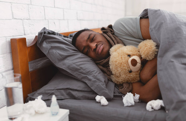 Deprimido Doente Africano Homem Abraçando Teddy Urso Deitado No Quarto - Foto, Imagem