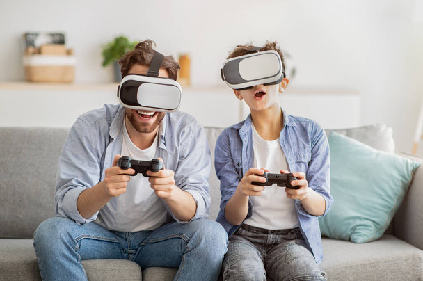 Virtuelle Realität. Aufgeregter Vater und Teenager-Sohn probieren VR-Brille aus und spielen gemeinsam Videospiele - Foto, Bild