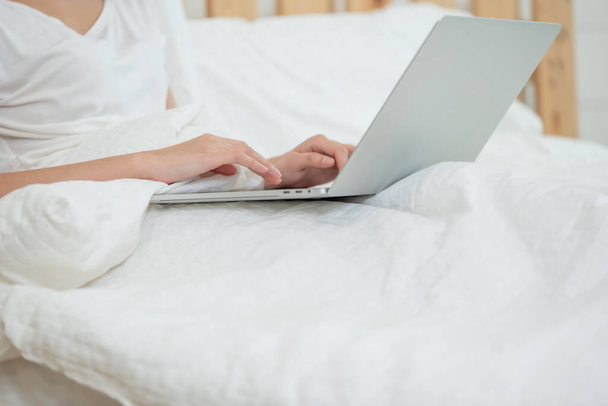 Close up of woman lying down on bed and using computer in bedroom - Foto, imagen