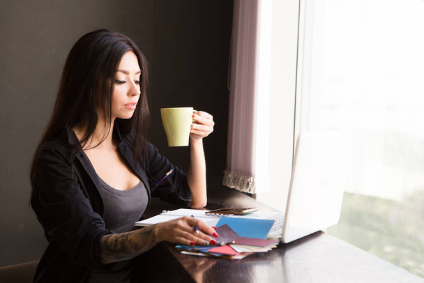 Beautiful young woman with coffee cup and laptop in the kitchen at hom. home office. - Foto, afbeelding