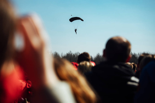 silhouettes of spectators against the background of landing parachutists. demonstration performances of skydivers jumping from a plane from a great height. extreme sports festival - Photo, Image