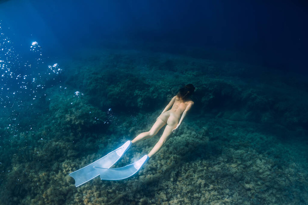 Γυμνή σπορ γυναίκα με ελεύθερα καταδυτικά πτερύγια βουτιά στον γαλάζιο ωκεανό. - Φωτογραφία, εικόνα