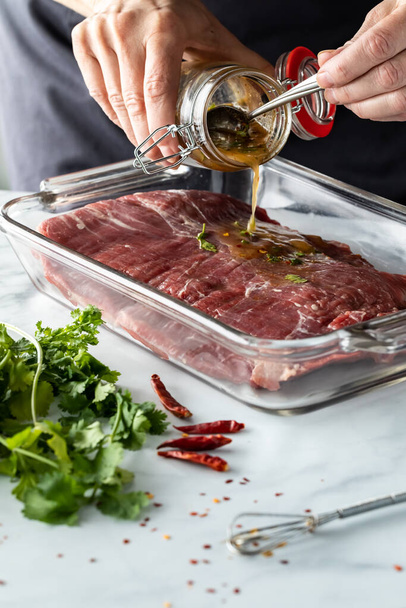 Close up of a chefs hands pouring marinade on a flank of raw beef. - Valokuva, kuva