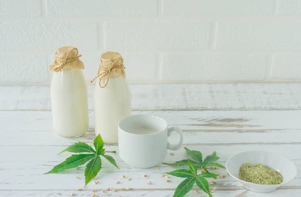 Flessen met Cannabis kruiden veganistische gluten en lactosevrije melk en cannabisbladeren op houten tafel. - Foto, afbeelding