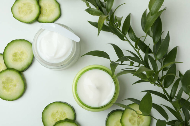 Jars with cosmetic cream, cucumber slices and branch on white table - Foto, immagini