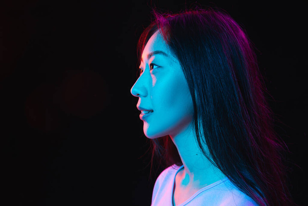 Asian young womans portrait on dark studio background in neon. Concept of human emotions, facial expression, youth, sales, ad. - Foto, immagini