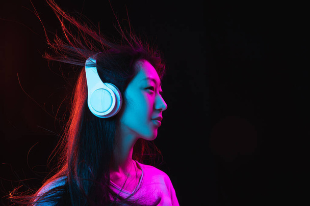 Azjatycki młody kobieta portret na ciemny studio tło w neon. Pojęcie ludzkich emocji, ekspresji twarzy, młodzieży, sprzedaży, reklamy. - Zdjęcie, obraz