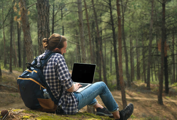 Young man sitting on ground at forest talking on smartphone and working on laptop . Workation concept. Intrnet 5G - Foto, Imagen