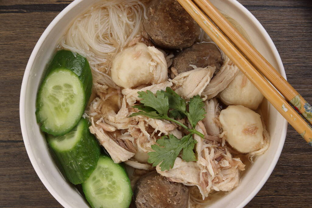 Clear white rice vermicelli beehoon noodle soup with chicken beef meat ball shredded cucumber in white bowl chopsticks spoon chili soya sauce parsley garnish - Photo, Image