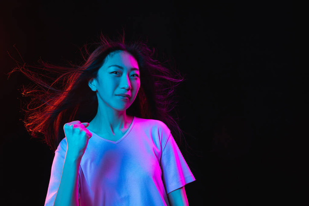 Asian young womans portrait on dark studio background in neon. Concept of human emotions, facial expression, youth, sales, ad. - Foto, immagini