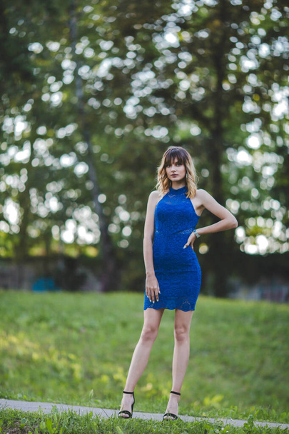 An attractive Bosnian lady wearing a blue dress and high heel shoes is posing in the park - Foto, Bild