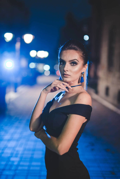 An attractive Caucasian female in a black sexy dress posing at camera in the night - Foto, imagen