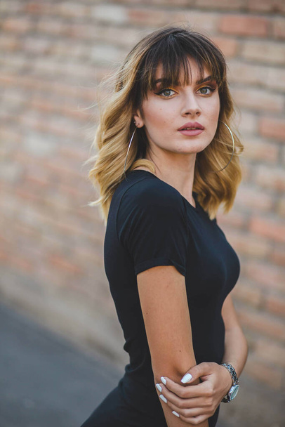 A beautiful Bosnian lady with expressive eyes wearing a black t-shirt and posing in the brick wall background - Photo, image