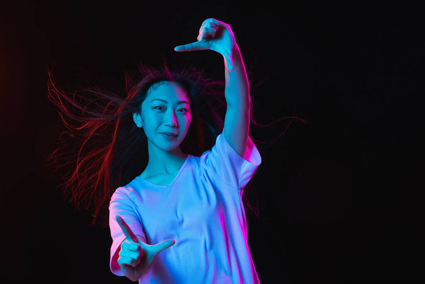 Asian young womans portrait on dark studio background in neon. Concept of human emotions, facial expression, youth, sales, ad. - Фото, изображение