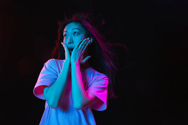 Asian young womans portrait on dark studio background in neon. Concept of human emotions, facial expression, youth, sales, ad. - Фото, зображення