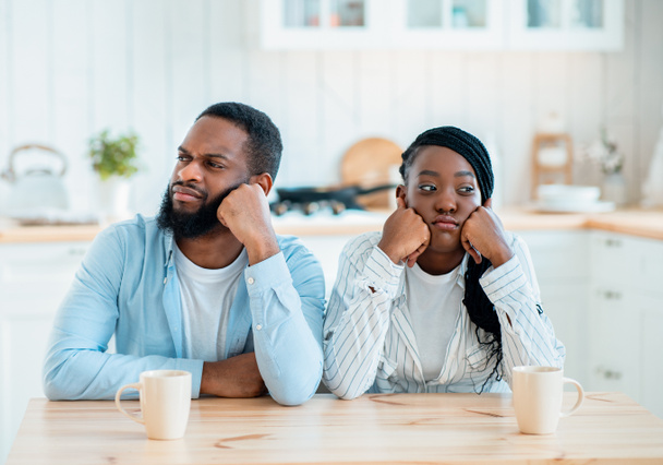Beziehungsprobleme. Beleidigtes schwarzes Paar sitzt am Tisch in Küche - Foto, Bild