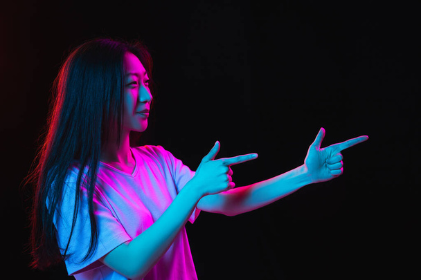 Asian young womans portrait on dark studio background in neon. Concept of human emotions, facial expression, youth, sales, ad. - Valokuva, kuva