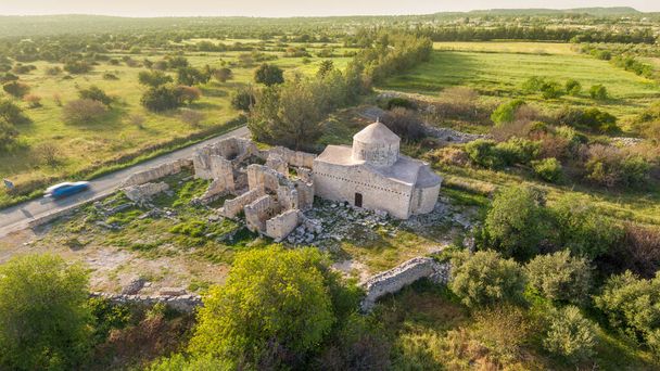Aerial view of medieval Timios Stavros (Holy Cross) monastery in Anogyra, Cyprus.  Renovated 15th century church and older Byzantine ruins over green fields landscape - Photo, Image