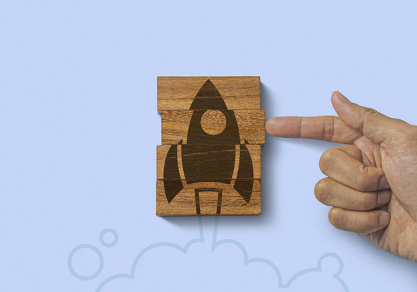 Hand putting the last piece of wooden blocks with launching rocket graphic icon on blue background. Business start up, start, new project or new idea concept. - Foto, Imagem