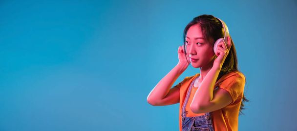 Asian young womans portrait on blue studio background in neon. Concept of human emotions, facial expression, youth, sales, ad. - Фото, зображення