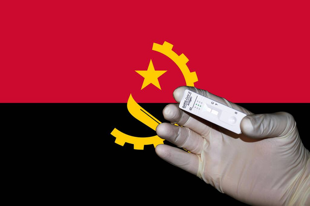 A hand showing a negative antigenic corona rapid test in front of a Flag of Angola. - Foto, afbeelding